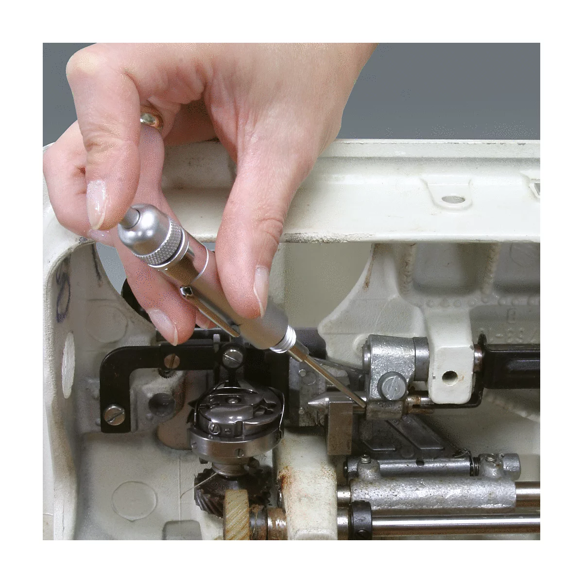 Eine Hand hält einen Schraubendreher und repariert eine Nähmaschine. Detailaufnahme, Nahaufnahme.